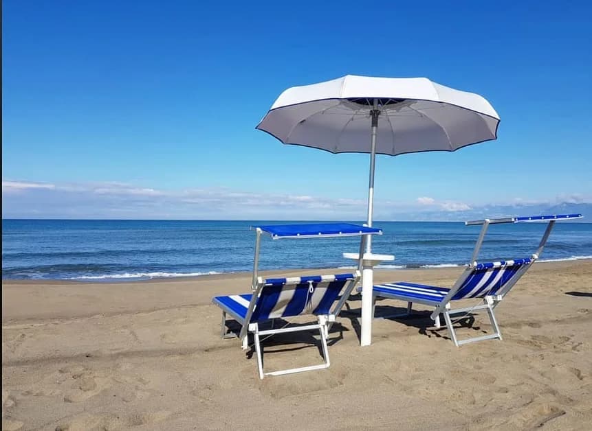 Ombrellone bianco e due lettini a righe blu con parasole sulla spiaggia