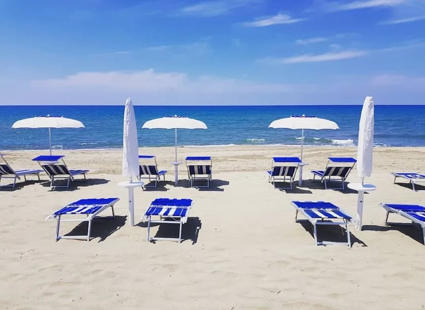 Spiaggia attrezzata con ombrelloni bianchi e lettini blu a righe